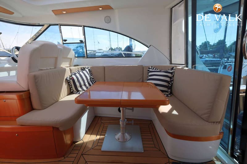 Een interieur van een boot met een U-vormige bank, een houten tafel en gestreepte kussens. — Beneteau Flyer 12 Cabin