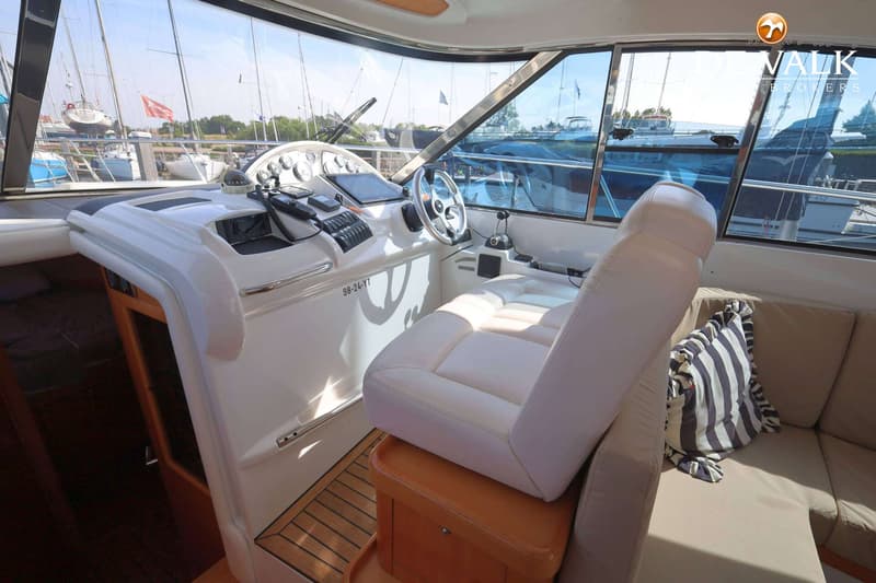 De foto toont het interieur van een boot met een stuurstand, een witte stoel en een bank met een gestreept kussen.