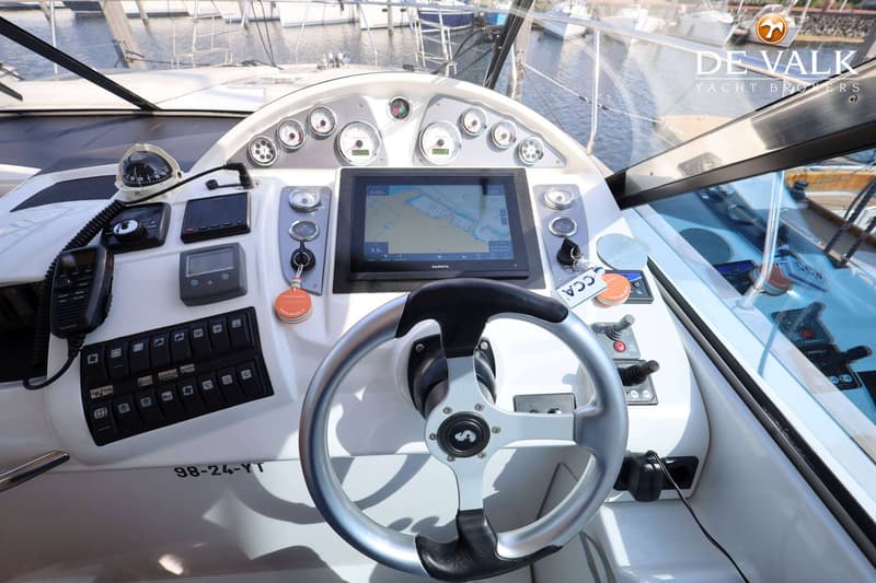 De foto toont het dashboard van een boot met een stuurwiel, navigatiescherm, meters, schakelaars en een marifoon.