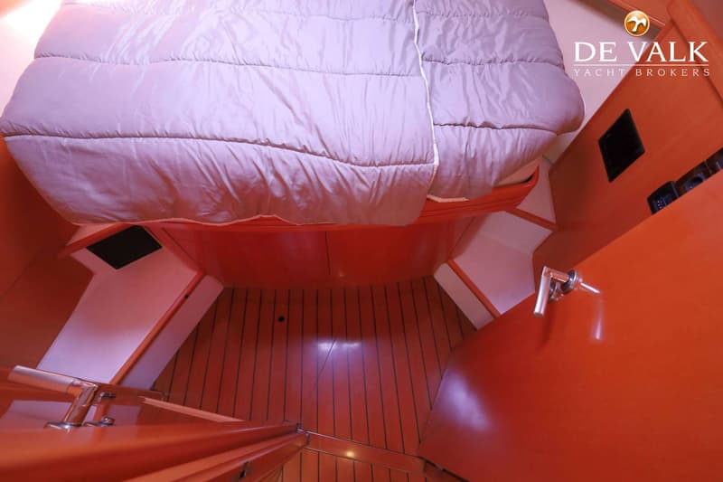 Een kajuit met een bed, houten vloer en oranje en witte wanden, met een deurklink rechts. — Beneteau Flyer 12 Cabin