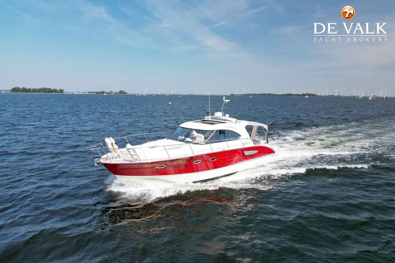 Een witte en rode motorboot vaart op open water met een man aan het roer, met windmolens op de achtergrond.