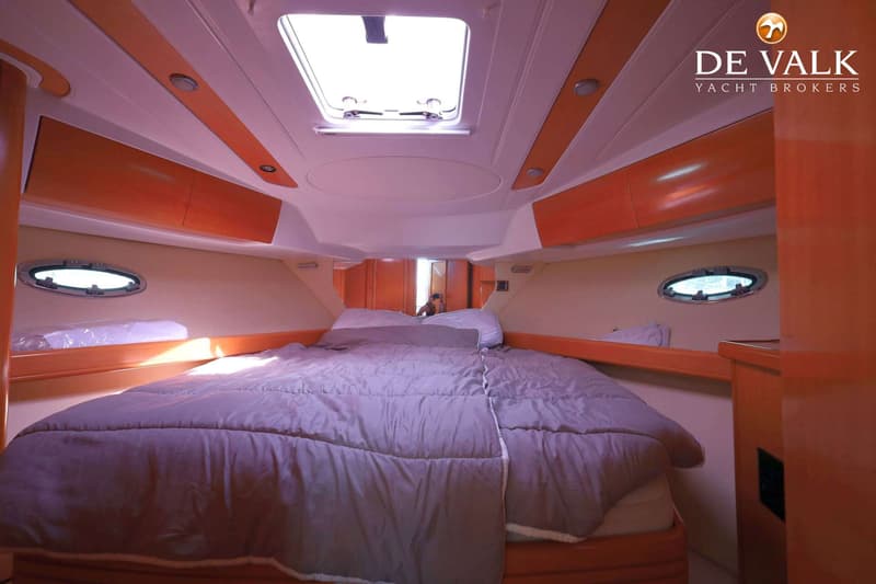 De foto toont een kajuit met een tweepersoonsbed, een dakraam, patrijspoorten en houten kasten. — Beneteau Flyer 12 Cabin