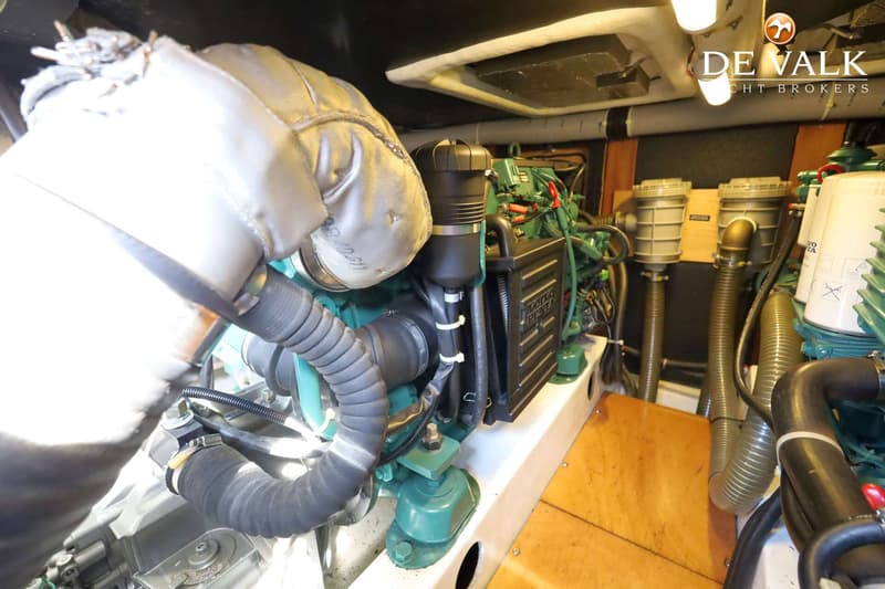 Een detailfoto van een scheepsmotor met diverse slangen, filters en bedrading, met een "De Valk Yacht Brokers" logo…