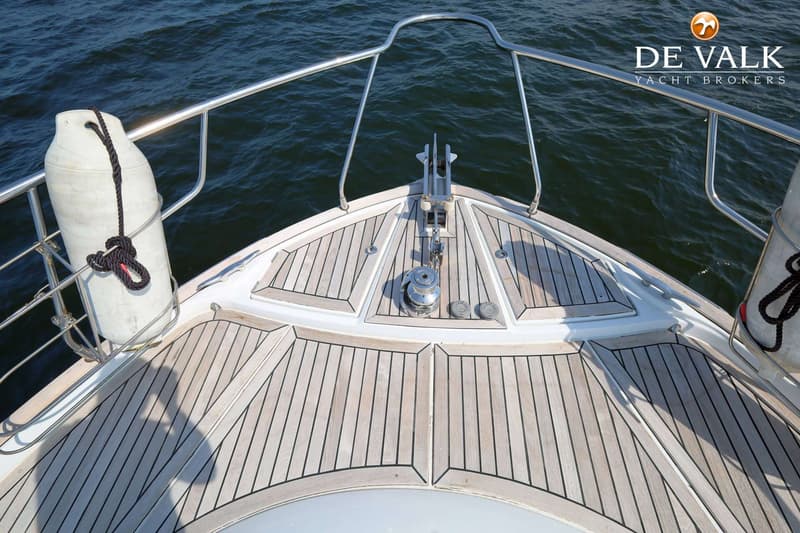 De boeg van een boot met een teakhouten dek, een ankerlier, een anker en een witte stootwil. — Beneteau Flyer 12 Cabin