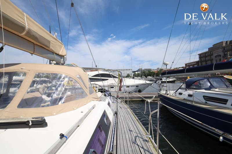 Een zeilboot met een beige buiskap en een houten dek ligt afgemeerd in een haven met andere boten. — Dufour 485 Grand Large