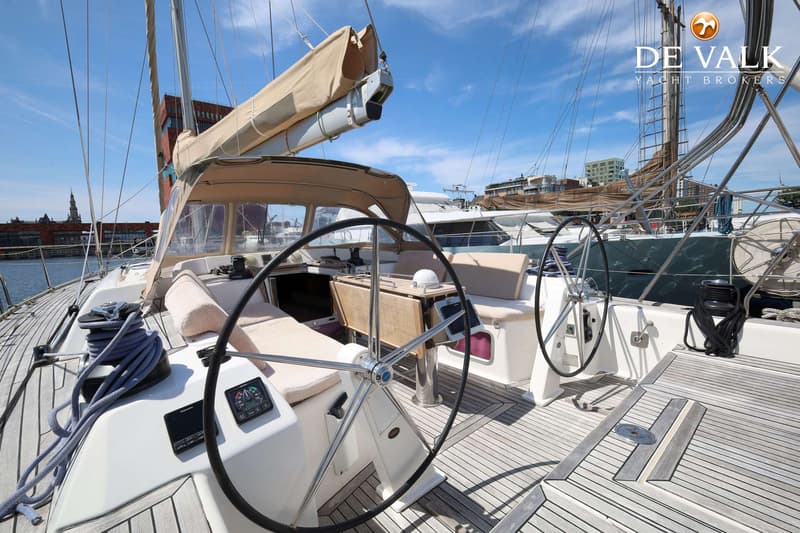 De foto toont de kuip van een zeilboot met twee stuurwielen, een houten tafel en een beige buiskap. — Dufour 485 Grand Large