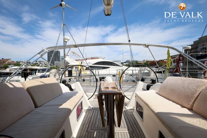 De foto toont de kuip van een zeilboot met twee stuurwielen, een houten tafel en beige kussens. — Dufour 485 Grand Large