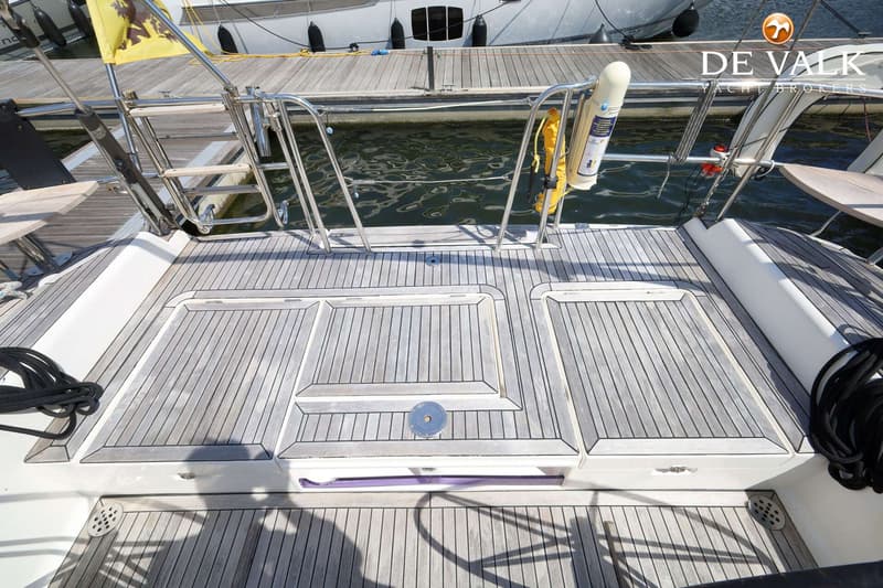 De foto toont het achterdek van een boot met teakhouten vloer, een zwemtrap, reling en een reddingsboei.