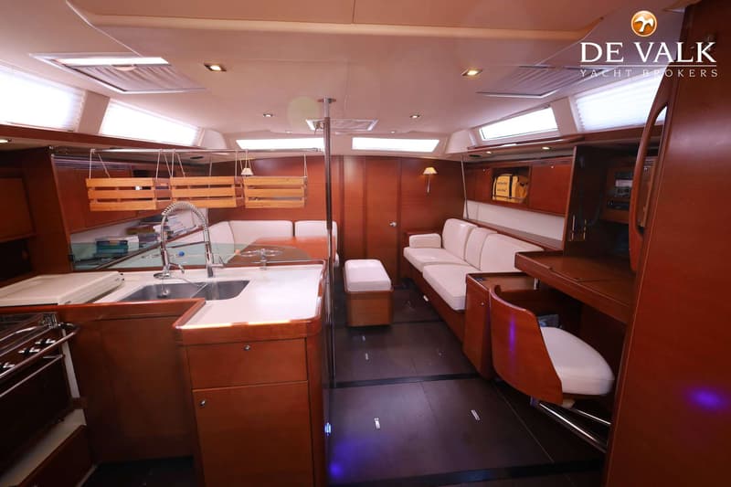De foto toont het interieur van een boot met een kombuis, zithoek, navigatiehoek en houten afwerking.