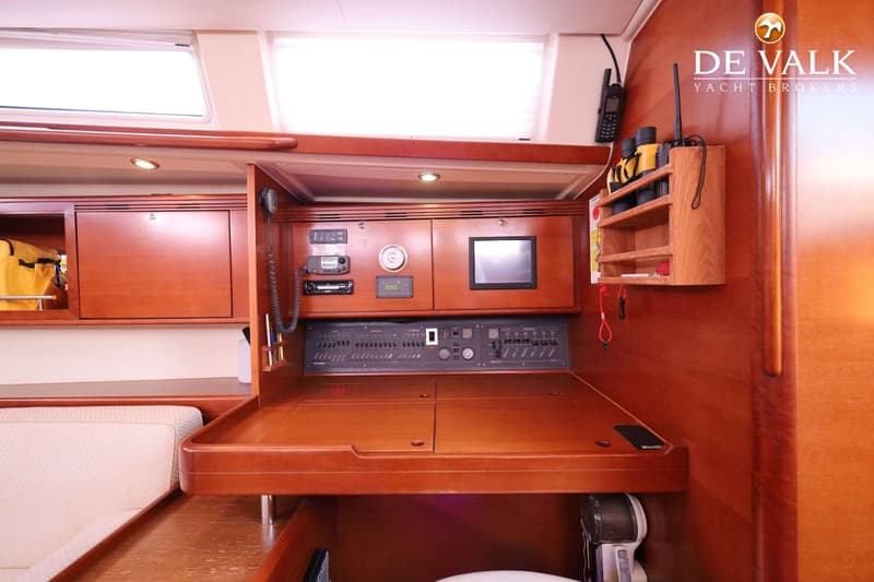 Een houten navigatiehoek met diverse instrumenten, schakelaars en een monitor, met een opbergrekje ernaast.