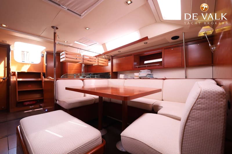 Een interieur van een boot met een houten tafel omringd door crèmekleurige banken en krukken, met houten kasten en planken.