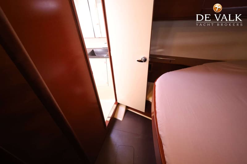 Een interieurfoto van een boot met een bed met roze laken, een open deur en een gootsteen. — Dufour 485 Grand Large