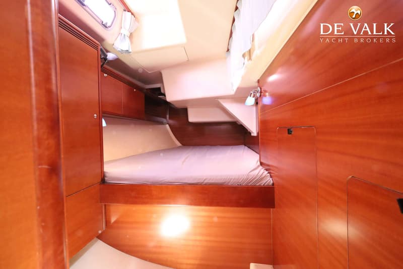 De foto toont een kajuit met een bed, houten kasten en panelen, en een raam met gordijnen. — Dufour 485 Grand Large