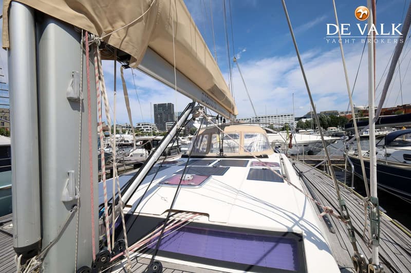 Een bovenaanzicht van het dek van een zeilboot met een mast, giek, zeilhuik, lieren en touwen, liggend in een haven.