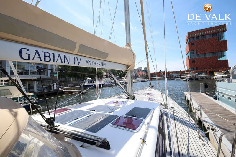 Een zeilboot met de naam "GABIAN IV ANTWERPEN" ligt aangemeerd, met zonnepanelen op het dek en een gebouw op de achtergrond.