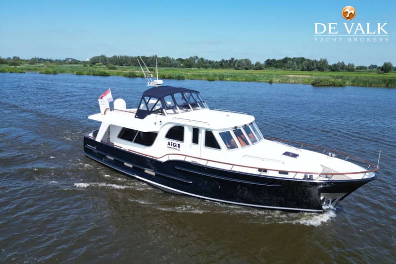 Een donkerblauwe en witte motorboot met de naam "AEGIR" vaart op een rivier met groene oevers onder een blauwe lucht.