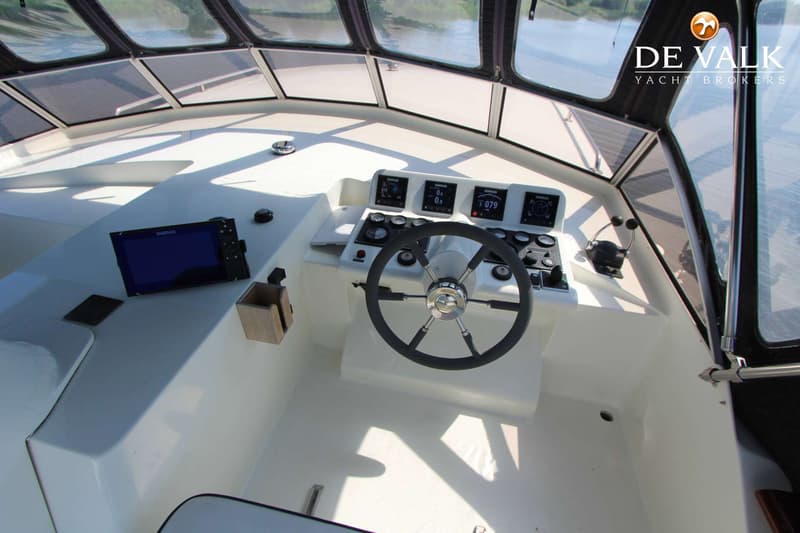 Een stuurhut met een stuurwiel, diverse meters, een Simrad scherm en een gashendel.