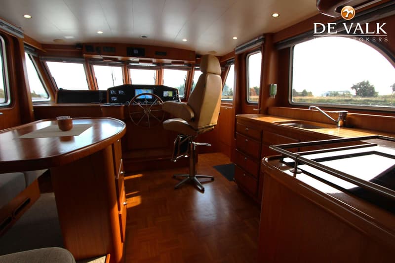Een interieur van een boot met een stuurstand, een tafel met banken, een keukenblok en houten vloer. — Vripack Searocco 1500