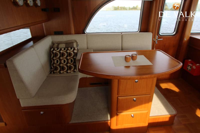 Een interieur van een boot met een houten tafel, een beige bank en ramen met uitzicht op water. — Vripack Searocco 1500