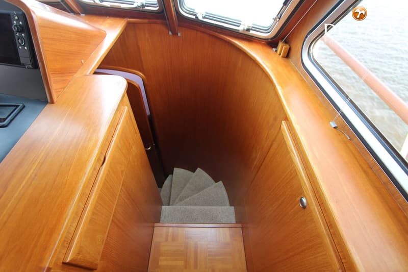 Een houten interieur van een boot met een trap naar beneden, ramen en een bedieningspaneel. — Vripack Searocco 1500