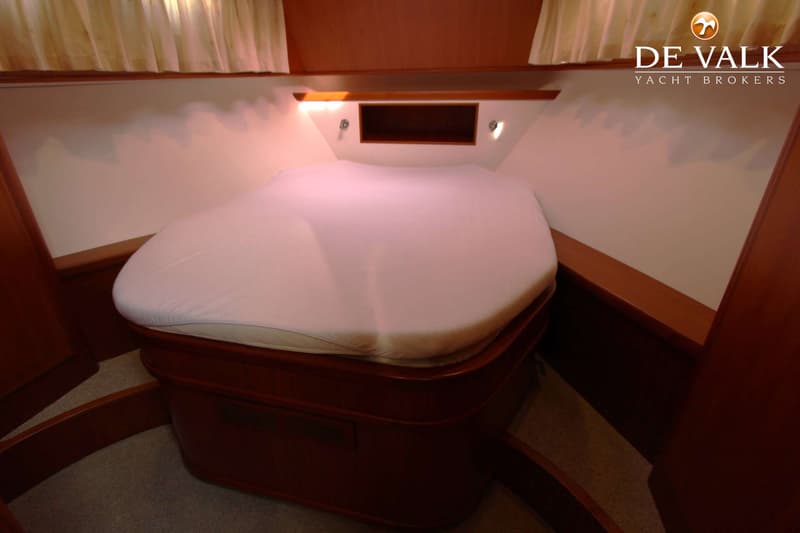 Een kajuit met een bed met wit hoeslaken, houten meubilair, twee leeslampjes en een nis. — Vripack Searocco 1500