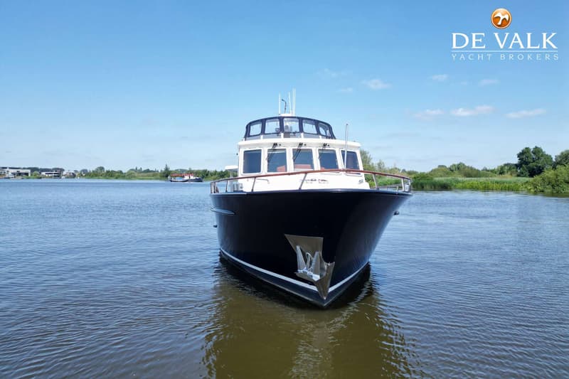 Een donkerblauwe motorboot met witte opbouw en een anker aan de boeg, drijvend op water onder een blauwe lucht.