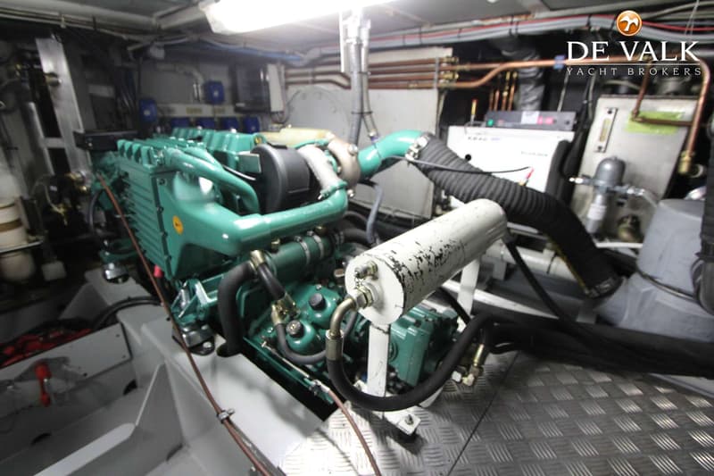 Een groene scheepsmotor met diverse slangen en leidingen, staand op een metalen vloer met ruitpatroon.
