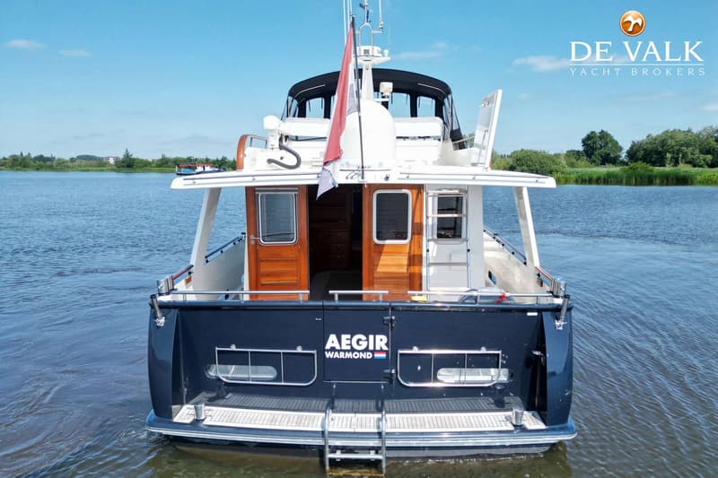 Een donkerblauwe boot met de naam "AEGIR WARMOND" op de spiegel, gezien vanaf de achterkant op het water.