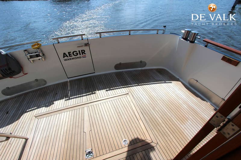 De foto toont het achterdek van een boot met een houten vloer, reling en de naam "AEGIR WARMOND" op de achterwand.