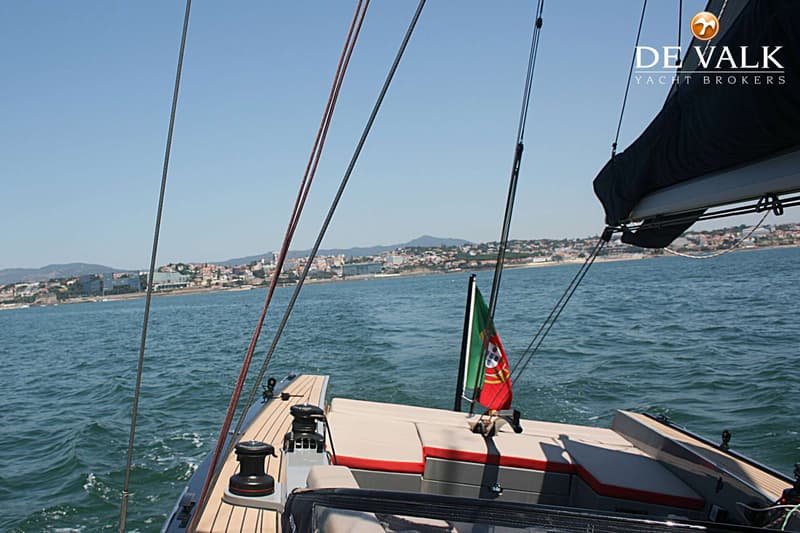 Een Portugese vlag wappert aan de achterkant van een boot met een houten dek en beige kussens, varend op zee.