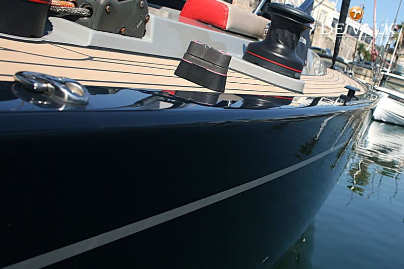 Een close-up van de zijkant van een donkerblauwe boot met een teakdek en een lier, liggend in het water.