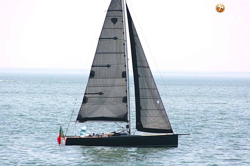 Een donkere zeilboot met twee zwarte zeilen en een Portugese vlag aan de achtersteven vaart op kalm water.