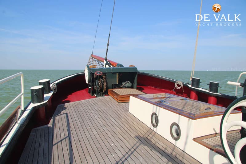 Een dek van een boot met een ankerlier, bolders, een kajuitingang en een stuurwiel, met water en windmolens op de…