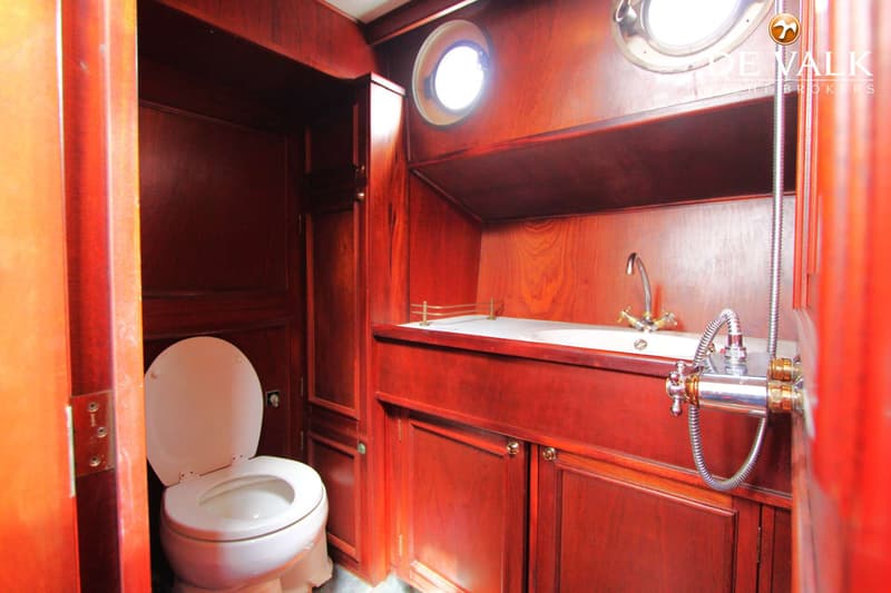 Een badkamer met een toilet, wastafel, douche en houten wanden en kasten.