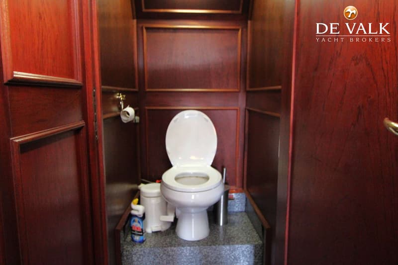 Een witte toiletpot met open deksel staat op een verhoogd grijs plateau in een ruimte met donkerhouten wanden.