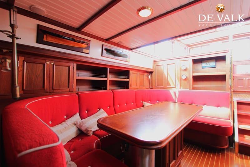 Een interieur van een boot met rode banken, een houten tafel en houten kasten en panelen. — Tjalk Koopmans Welvaren