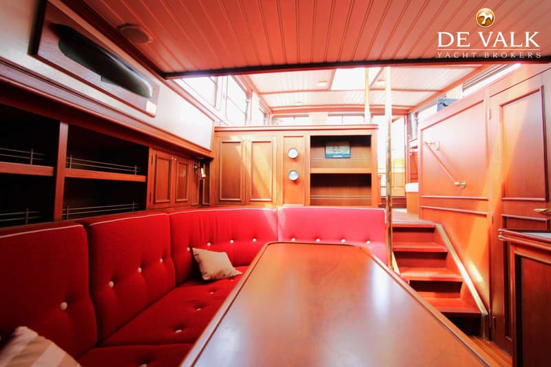 Een interieur van een boot met rode banken, een houten tafel en houten kasten en wanden. — Tjalk Koopmans Welvaren