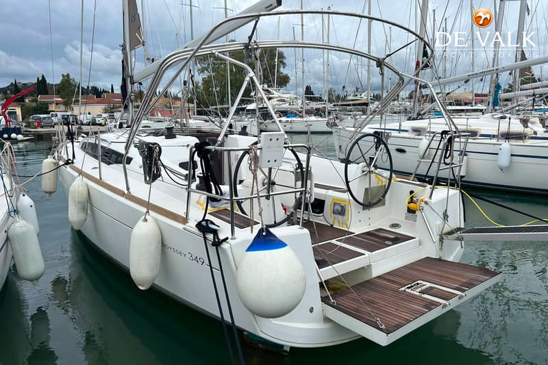 Een witte zeilboot met de tekst "ODYSSEY 349" op de zijkant, ligt afgemeerd in een haven. — Jeanneau Sun Odyssey 349