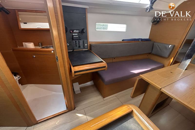 De foto toont een interieur van een boot met houten afwerking, een bank met kussens, een navigatiepaneel en een kleine…