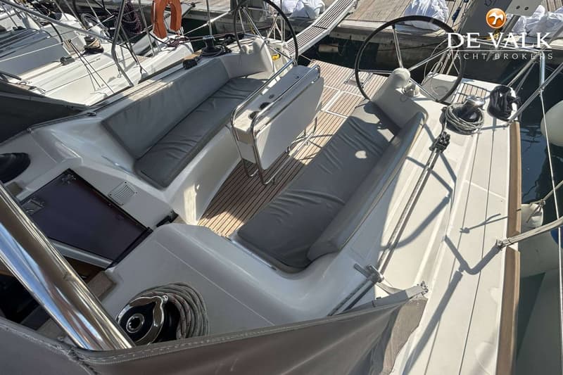 De foto toont de kuip van een zeilboot met twee stuurwielen, een houten vloer en grijze kussens op de banken.