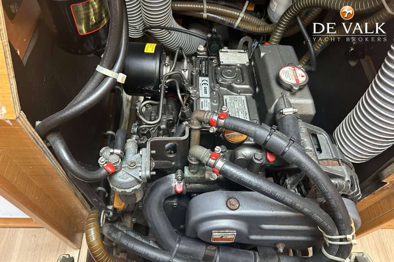 Een close-up van een Yanmar scheepsmotor met diverse slangen, leidingen en een waarschuwingssticker.