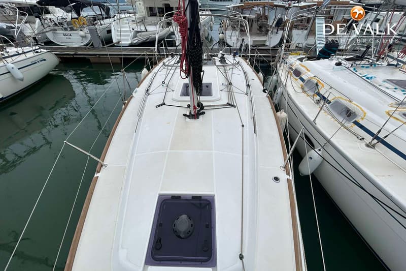 Een bovenaanzicht van het dek van een witte zeilboot met een mast, luiken en relingen, omringd door andere boten in een…