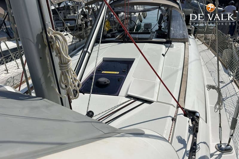 Een dek van een zeilboot met een luik, touwen en een mast, met een "DE VALK YACHT BROKERS" logo rechtsboven.