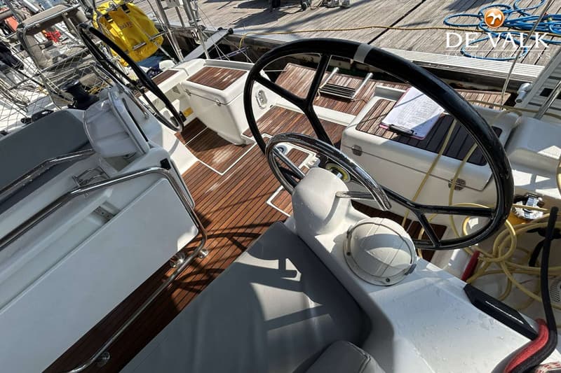 De foto toont de kuip van een zeilboot met twee stuurwielen, teakhouten vloer en grijze kussens. — Jeanneau Sun Odyssey 419