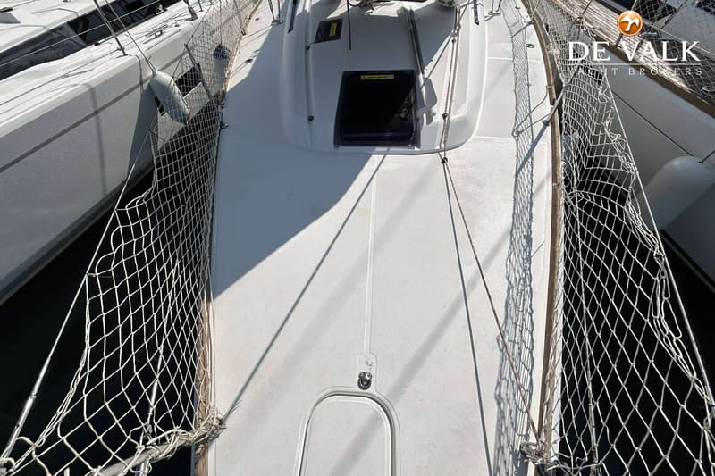 Een bovenaanzicht van het witte dek van een zeilboot met een luik en veiligheidsnetten aan beide zijden.