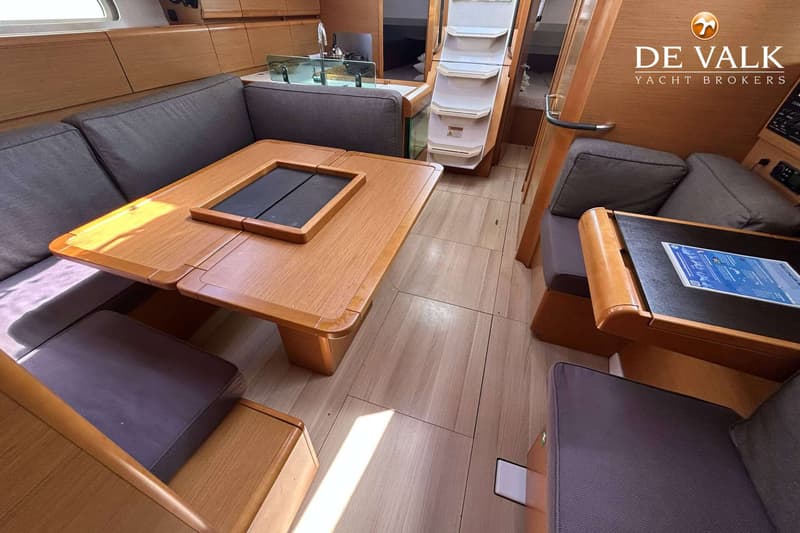 Een interieur van een boot met een houten tafel, grijze banken en een trap naar een lager dek. — Jeanneau Sun Odyssey 419