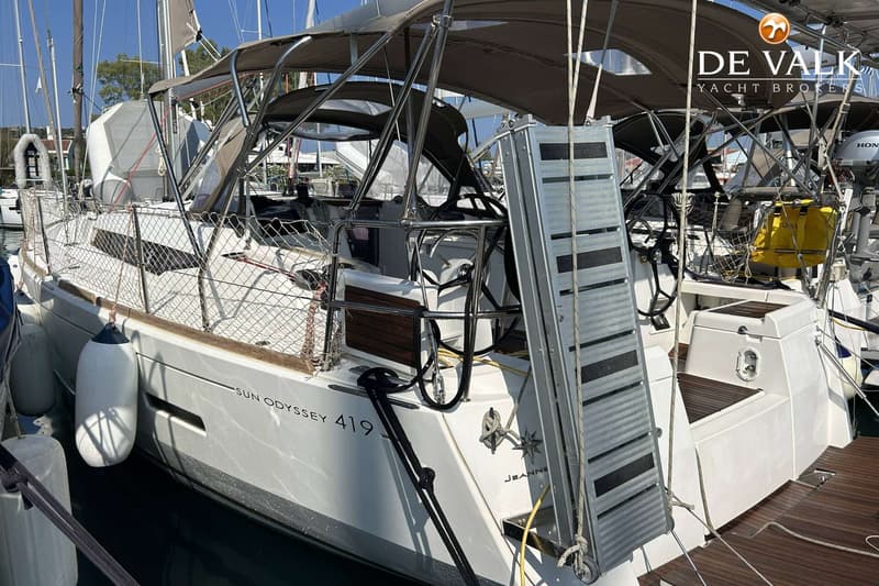 Een witte zeilboot met de naam "SUN ODYSSEY 419 JEANNEAU" ligt afgemeerd in een haven, met een loopplank aan de achtersteven.