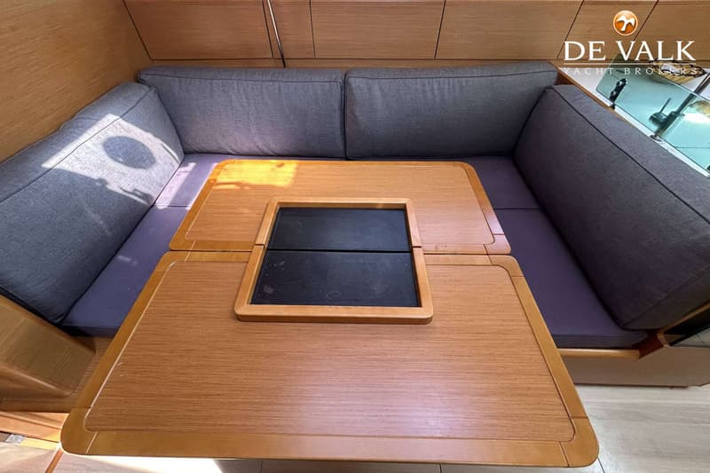 Een interieur van een boot met een U-vormige zitbank met grijze kussens en een houten tafel met een zwart inzetstuk.