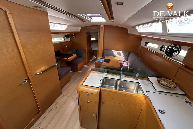 De foto toont het interieur van een boot met een kombuis, zithoek en doorgang naar een slaapcabine.