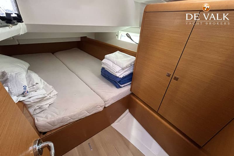 De foto toont een kajuit met twee bedden, een stapel handdoeken en een houten kast. — Jeanneau Sun Odyssey 419